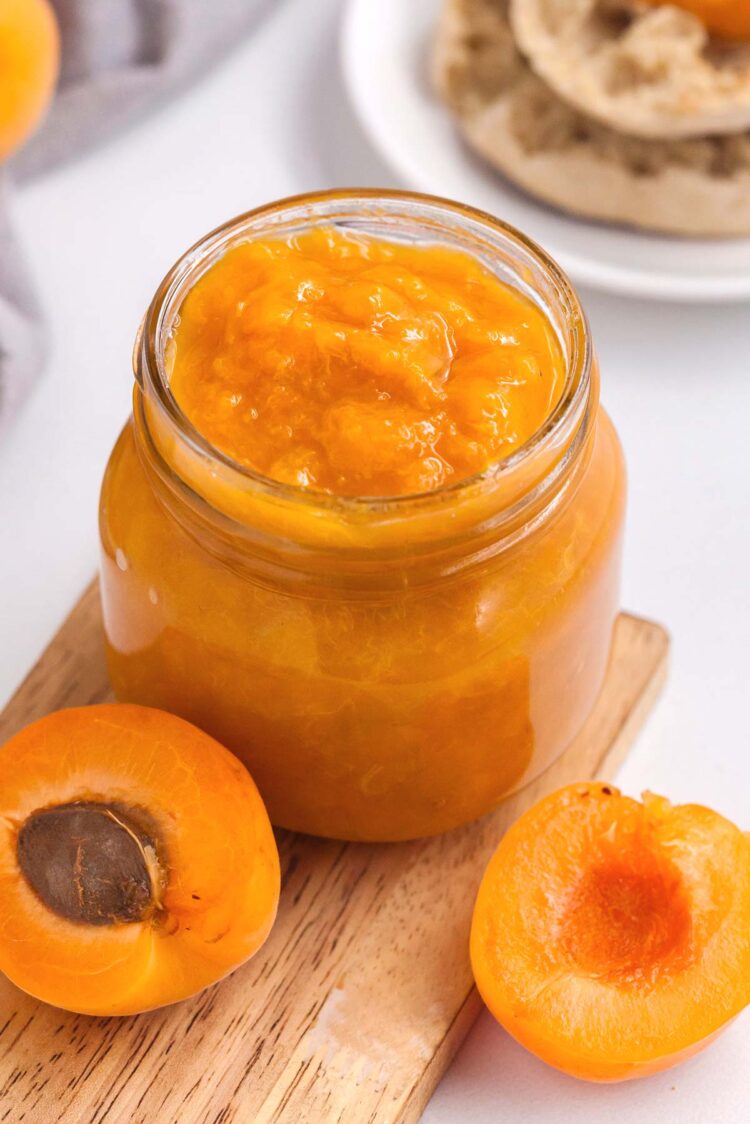 an open apricot and jar of apricot preserves on a wooden cutting board