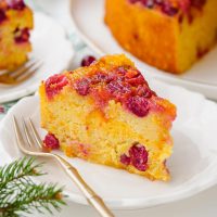 photo of a slice of whole orang cake with cranberries on a plate with a fork