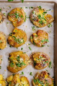 smashed Parmesan potatoes spread out on a white parchment on baking sheet
