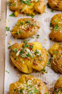 smashed Parmesan potatoes on a white parchment on baking sheet