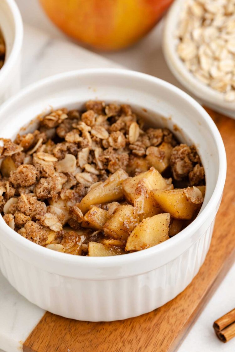 white ramekin filled with apple crumble on a wooden cutting board