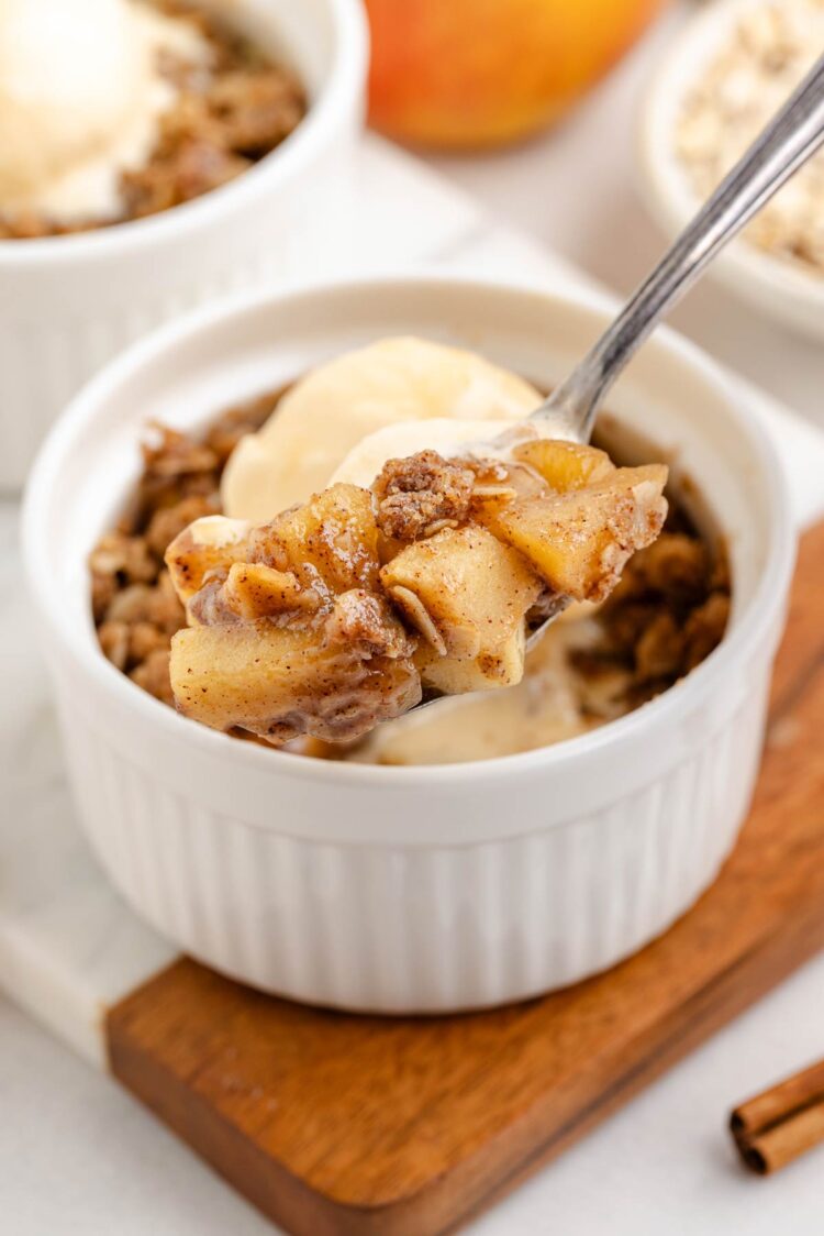 spoon digging into a ramekin of apple crumble for two with ice cream on top