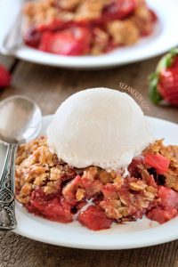 strawberry rhubarb crisp topped with vanilla ice cream on a white plate