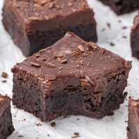 image of a gooey Baileys brownies with chocolate frosting and shaved chocolate shavings with one brownie with a bite taken out of it