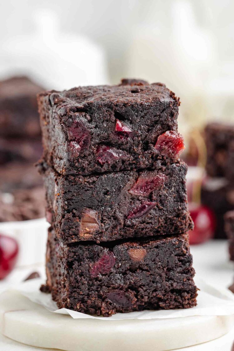 stack of 3 cherry brownies on a white table with more in the background