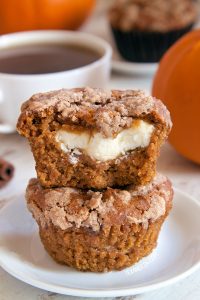stack of two pumpkin cream cheese muffins on a white plate, with a bite taken from the top muffin
