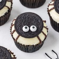 close up image showing a spider cupcake decorated with an Oreo cookie as the body of a spider with piped legs on cheesecake icing and cute candy eyes