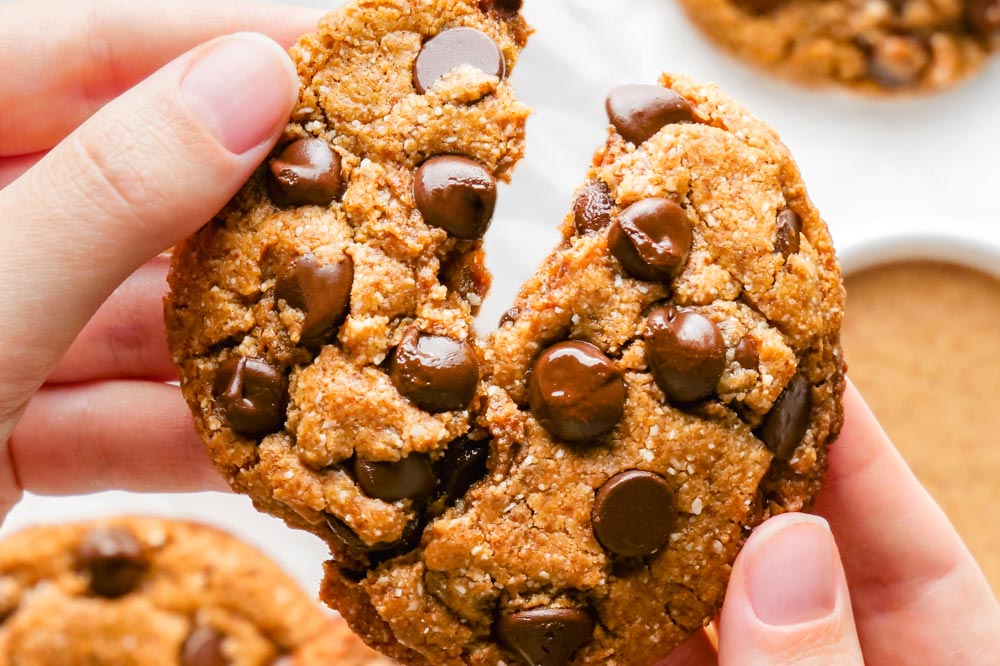 A hand pulling apart a paleo chocolate chip cookie.