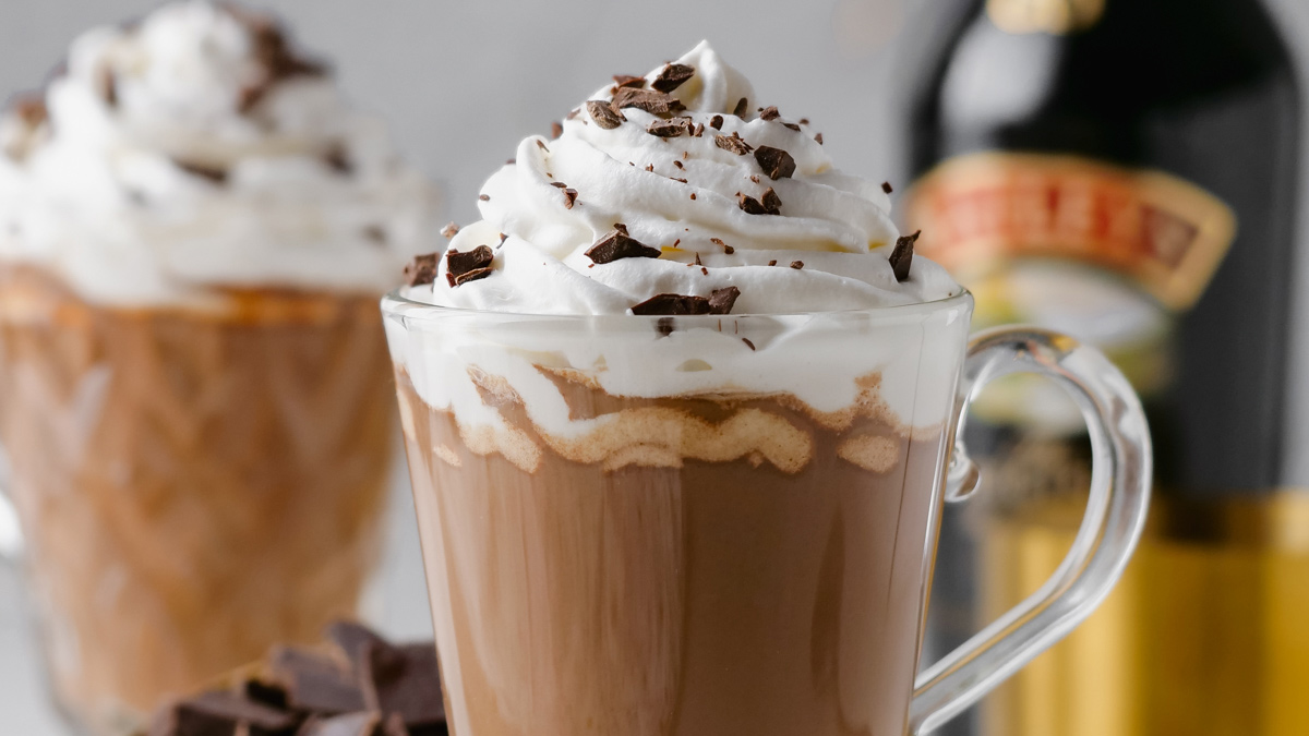 Mug of Baileys hot chocolate topped with whipped cream and shaved chocolate with a bottle of Baileys in the background.