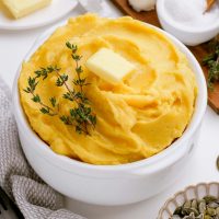 image of a bowl of squash mashed potatoes with a pat of butter and a sprig of thyme on top