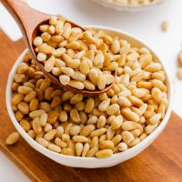 photo showing a bowl of toasted pine nuts with a wooden spoon