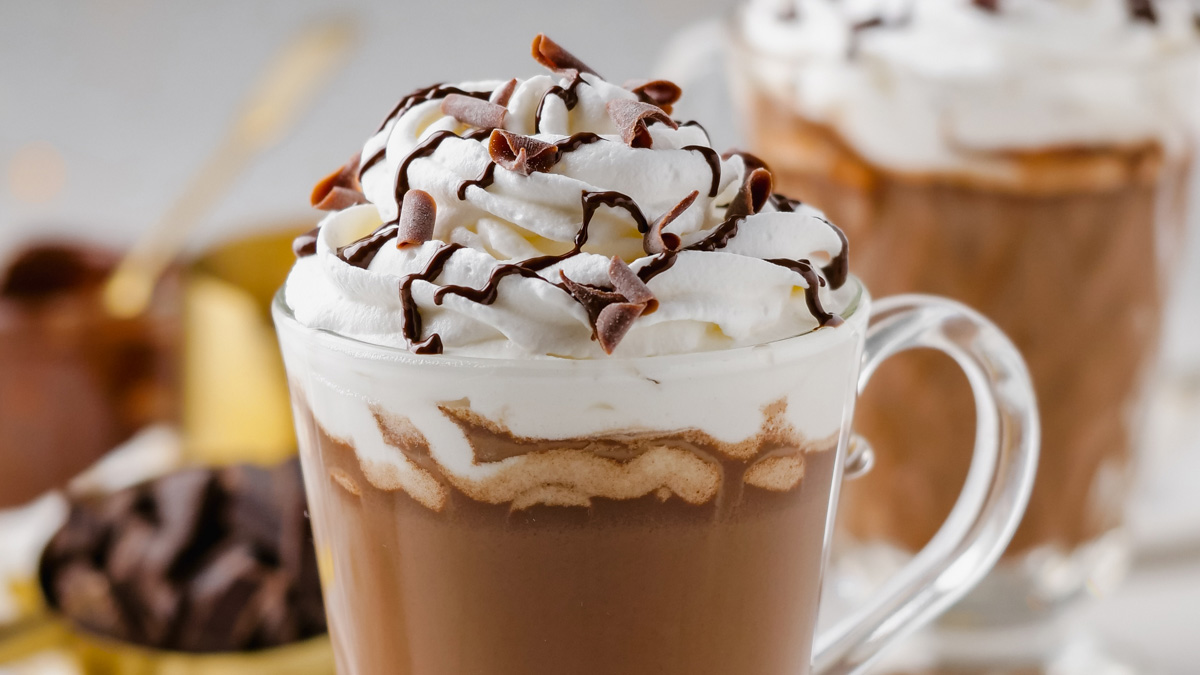 Vegan hot chocolate in a clear mug with whipped coconut cream and chocolate curls on top.