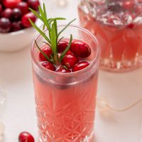 image of a tall glass of Christmas morning punch garnished with a sprig of rosemary and fresh cranberries