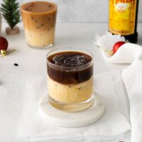 image of a glass of a perfectly layered eggnog white russian with a second glass and a bottle of Kahlua in the background
