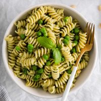 overhead view of green pea pasta in a white bowl with a fork to the side and garnished with fresh basil