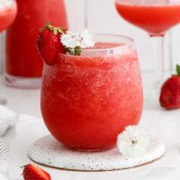image of a wine glass with frozen strawberry frosè garnished with a fresh strawberry and edible, white flower