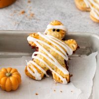 closeup photo of a gluten-free mummy hand pie decorated with white frosting stripes to look like bandages and two little eyes on a baking sheet with a little pumpkin to the side