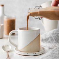 photo of a glass bottle pouring homemade vegan Baileys into a coffee mug