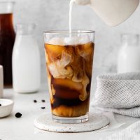 milk being poured into glass of cold brew