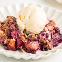 apple and blueberry crumble on a white plate with scoop of ice cream on top