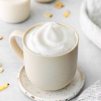 a mug of frothed almond milk on a saucer with scattered almond slivers in the background