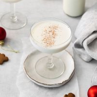 Alexander cocktail in a coupe glass dusted with nutmeg on a rustic plate and red baubles in the foreground