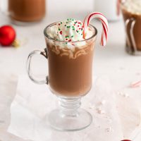 Christmas hot chocolate in an Irish coffee mug with whipped cream red and green sprinkles and a candy can in the mug