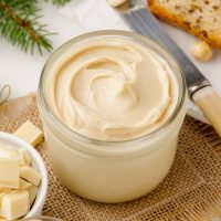 jar of creamy homemade white nutella with a ramekin of white chocolate in foreground and a knife in background