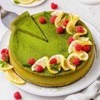 Top view of matcha cheesecake dusted with vibrant green matcha and decorated with twisted lemons and red raspberries