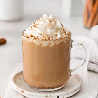 close-up of a glass mug with a dolce latte with whipped cream and dusting of cinnamon on a rustic plate