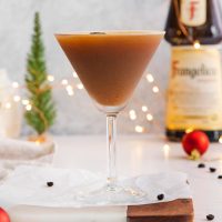 a martini glass full of Frangelico espresso martini with a bottle of Frangelico liqueur in the background and a small tree and twinkling lights