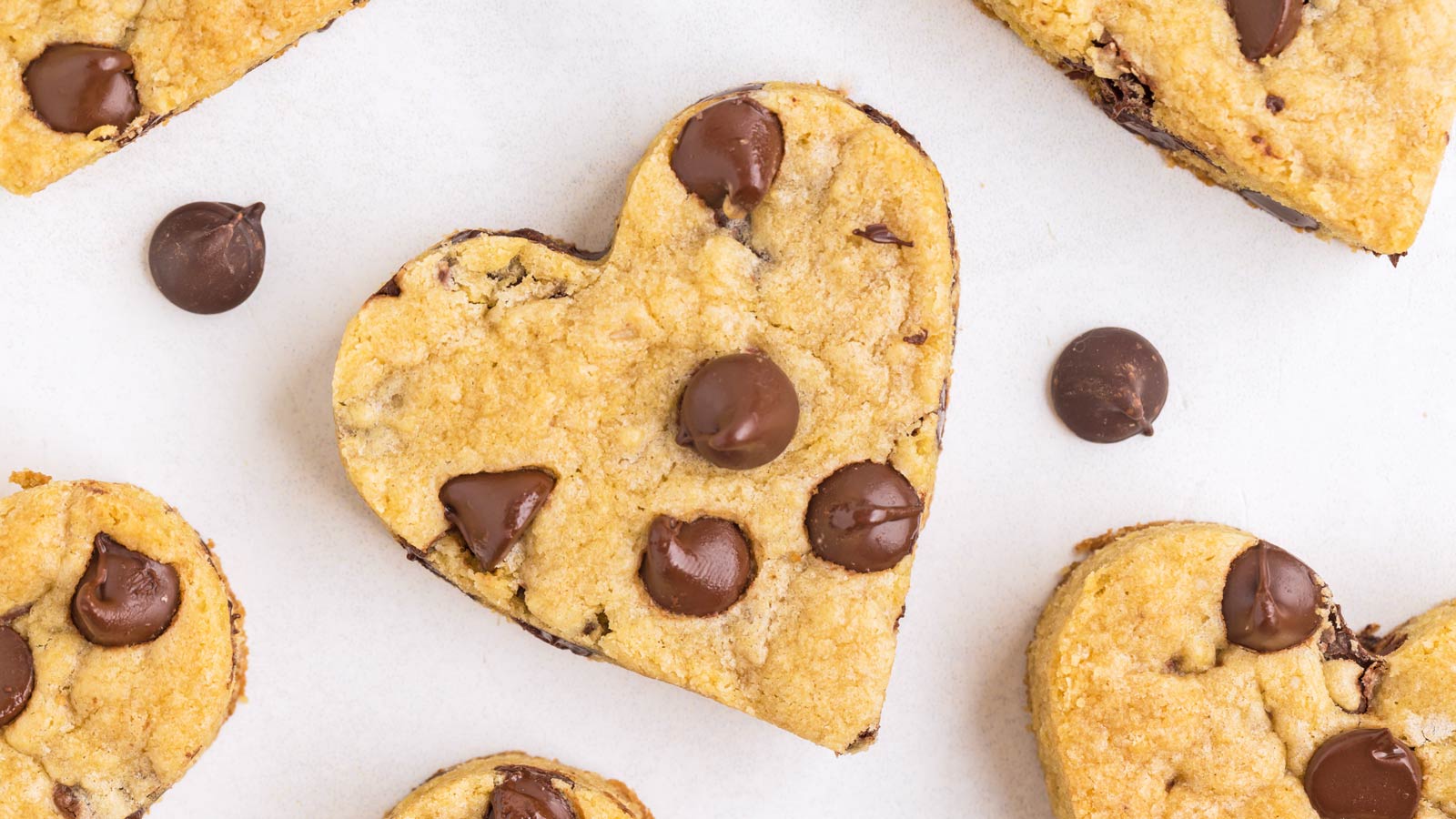 Heart-shaped chocolate chip cookies on a white piece of parchment paper.
