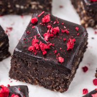 close up image of a vegan date brownie with chocolate topping and garnished with dried red raspberries