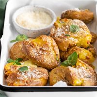 close up image of a white platter filled with golden air fryer smashed potatoes garnished with green parsley