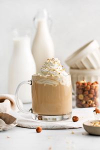 image showing a glass mug full of hazelnut latte, a Starbucks copycat recipe topped with whipped cream and bits of roasted hazelnuts