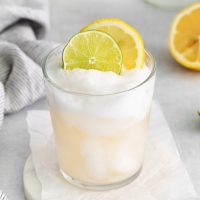 image of a tall boy glass with a slightly pink vodka sour topped with foamy egg white and garnished with wheels of lemon and lime