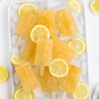 top view image of a stack of bright lemon popsicles on a tray with ice cubes and slices of lemons