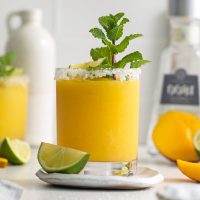 photo of a glass full of mangorita cocktail which is golden orange in color with a sprig of green mint and a lime wedge