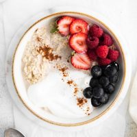 image of a white bowl full of overnight oats without chia seeds, but topped with yogurt, cinnamon, fresh blueberries, raspberries and sliced strawberries
