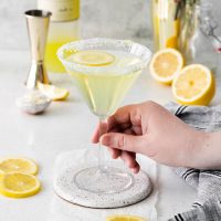 image of a hand picking up the stem of a glass full of limoncello martini garnished with a lemon wheel