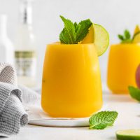 side view of a tall glass of a golden, orange glass of mango mule cocktail garnished with fresh mint and a lime wedge