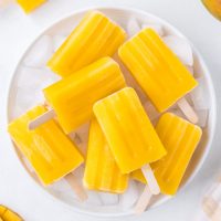 image of bright orange mango popsicles stacked on a white plate