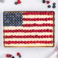 top view photo of red, white and blue cheesecake bars that is decorated like a USA flag with blue berries and fresh strawberries making the flag