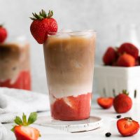 side view of a tall glass of a layered strawberry latte garnished with a fresh strawberry