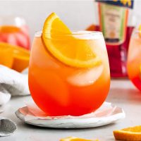 side view of an Aperol soda that is bright orange garnished with a slice of orange