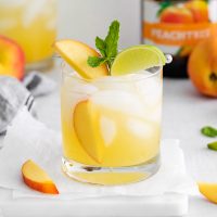 image of yellow Peachtree cocktail garnished with peach slices, lime and a sprig of mint