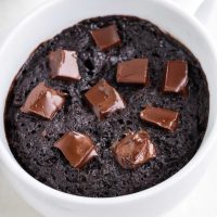 close up image of a protein powder mug cake topped with chocolate chips in a white mug