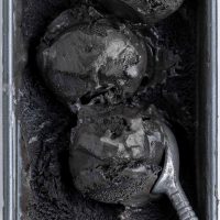 close up of two scoops of deep black ice cream and an ice cream scoop