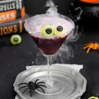 photo of a Halloween martini with smoke from dry ice rising from the rim and melon and blueberry eyeballs floating in the glass