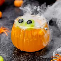 image of a glass of rum punch for Halloween garnished with eyeballs made with melon and blueberries and dry ice giving it a smokey effect on a dark black background